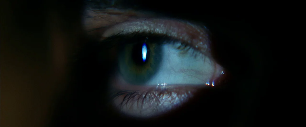 Days of Thunder (1990) movie still: closeup — A close-up view of a single human eye peering through a dark aperture. The pupil catches a sharp…