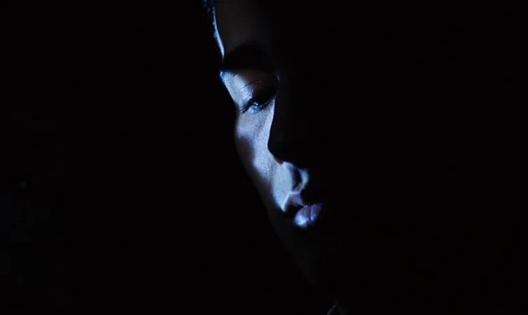 The Rose King (1986) movie still: closeup — A dimly lit space obscured by extreme shadow. A person face is partially visible in profile.