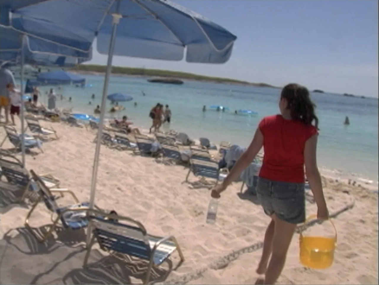 All Aboard! Rosie's Family Cruise (2006) movie still: medium — A crowded sandy beach with numerous blue umbrellas and lounge chairs under a clear…