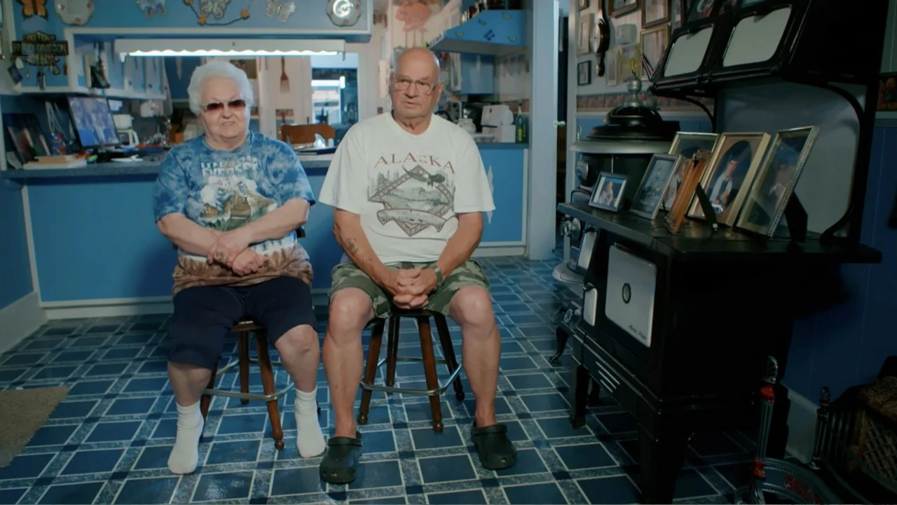 Mommy Dead and Dearest (2017) movie still: medium — A residential room features blue walls, tiled floors, and various framed family photographs…