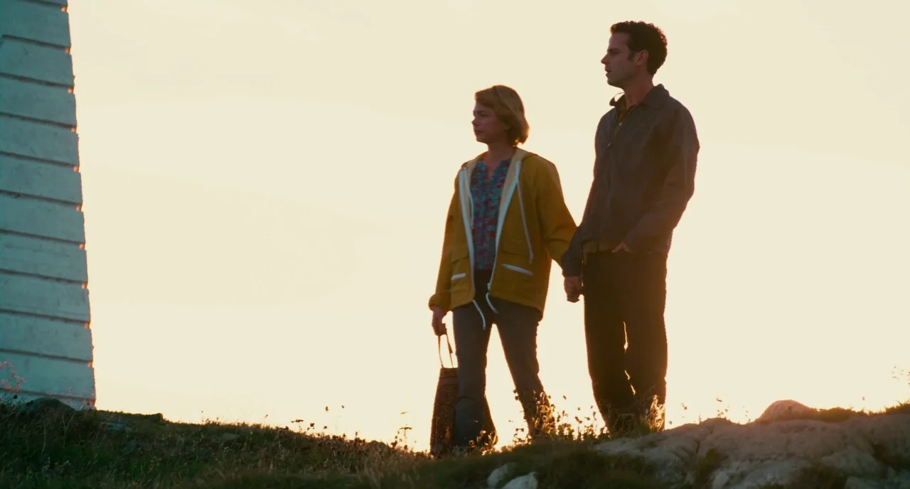 Take This Waltz (2011) movie still: fullbody — An grassy cliffside ridge overlooks a vast expanse under a bright setting sun. A woman and man walk…