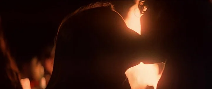 Jaws movie still: closeup — A dark, underexposed space is defined by a singular, intense source of backlight. Two silhouettes lean into one another…