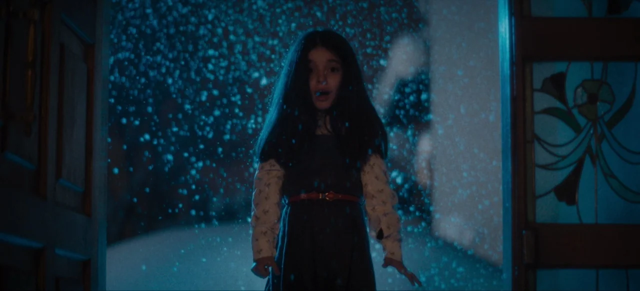 Housewife (2017) movie still: medium — A dark, snow-filled exterior seen through an open doorway at night. A young girl stands framed in the doorway…