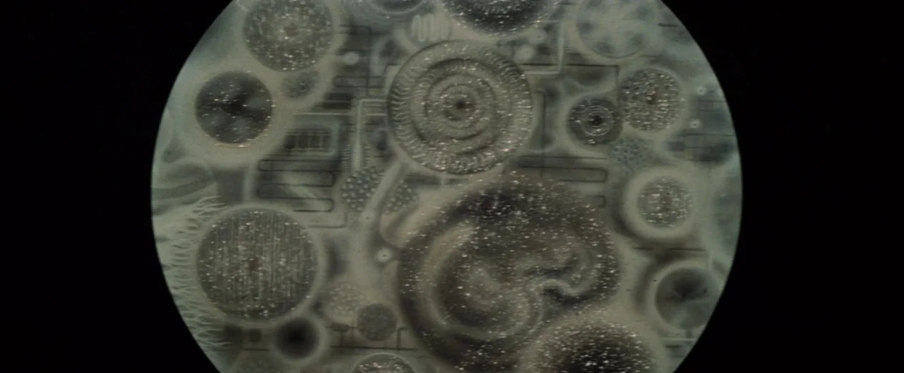 Destroy All Monsters (1968) movie still: closeup — A circular view through a microscope reveals intricate, swirling patterns of organic biological…