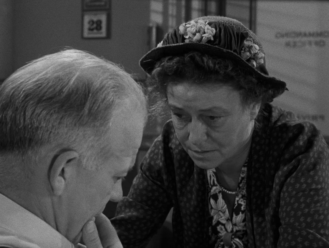 Pickup on South Street (1953) movie still: medium — A mid-century office interior with a calendar marked twenty-eight hanging on the rear wall. A…