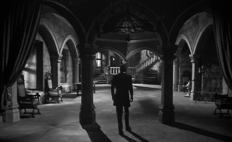 Black Sunday (1960) movie still: fullbody — A spacious castle stone interior features gothic arches and a central staircase background. A man in a…