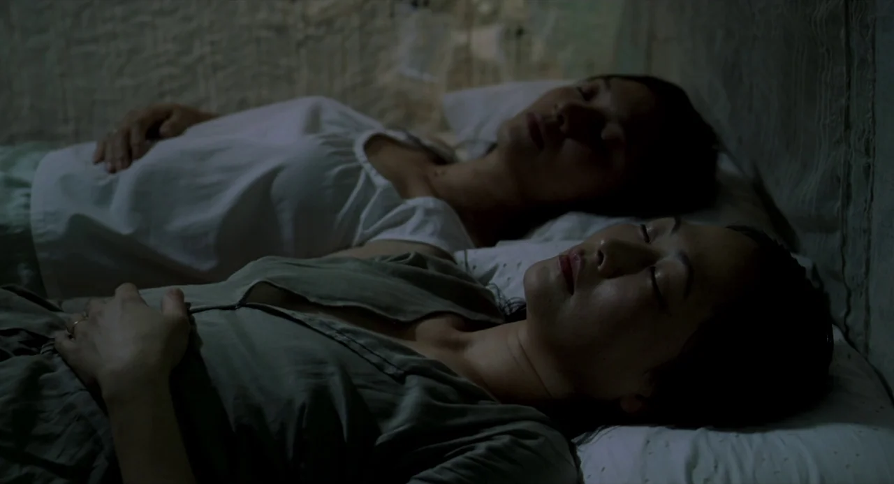 The Vertical Ray of the Sun (2000) movie still: medium — A dimly lit room features two women lying side by side on a bed. They are resting with…