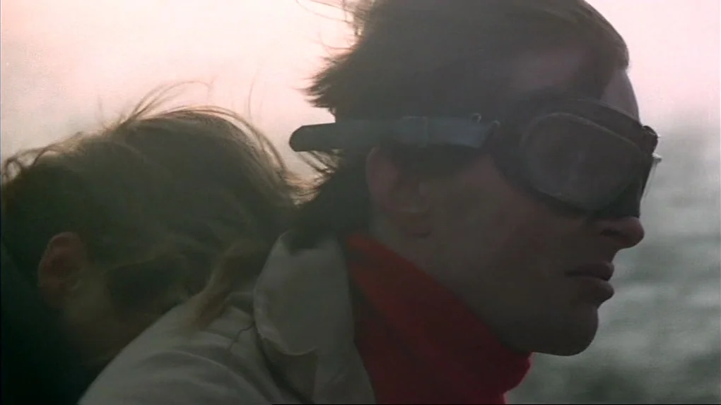 The Sorcerers (1967) movie still: closeup — A man and woman ride a motorcycle through a hazy, bright outdoor environment. The man wears classic…