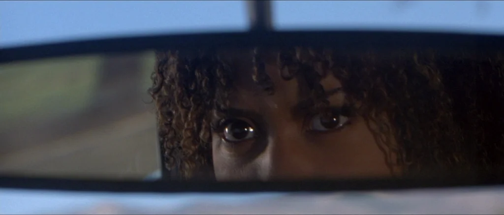 Death Proof movie still: closeup — A close-up view through a car rearview mirror showing a woman's eyes. The subject watches the reflection with an…