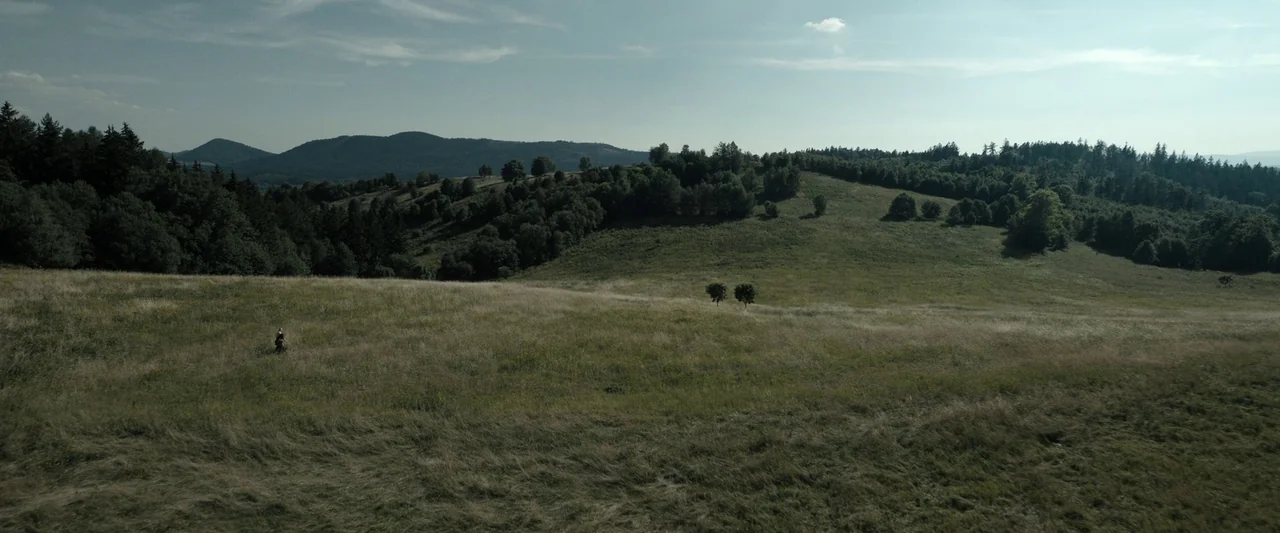 The Hunger Games: The Ballad of Songbirds & Snakes (2023) movie still: wide — A vast, rolling meadow stretches toward dense forests and distant,…