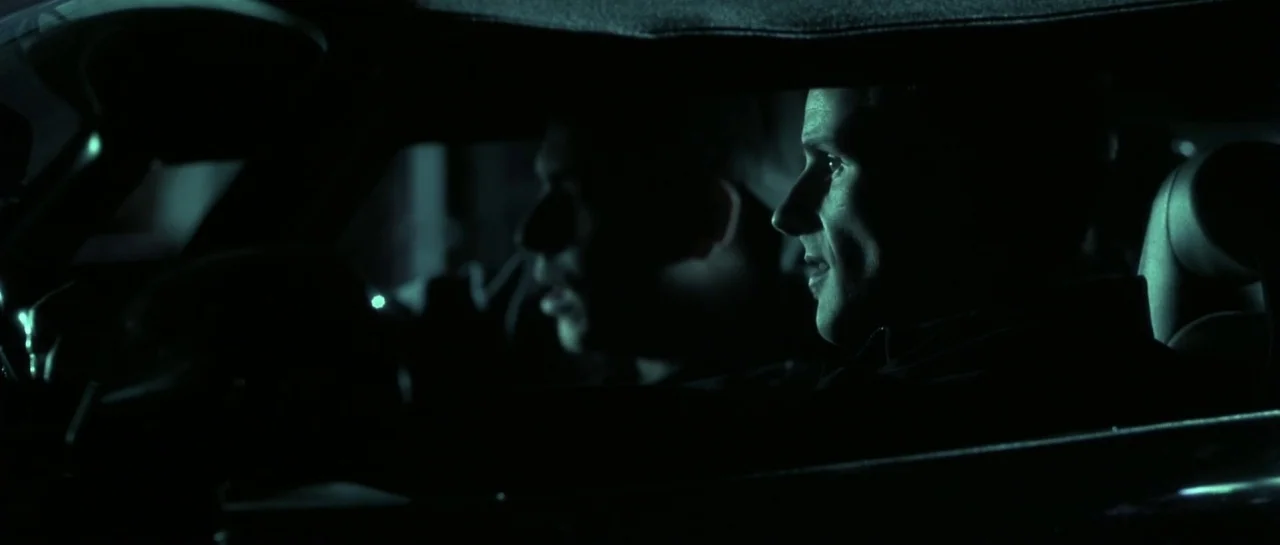 Bones movie still: medium — A dark vehicle cabin at night with occupants seen in profile. Faint green light catches the face of the man on the right.