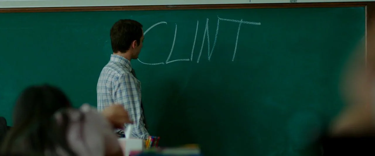 Cooties (2014) movie still: medium — A green chalkboard occupies the frame with the name Clint written in white chalk. A man in a dress shirt stands…