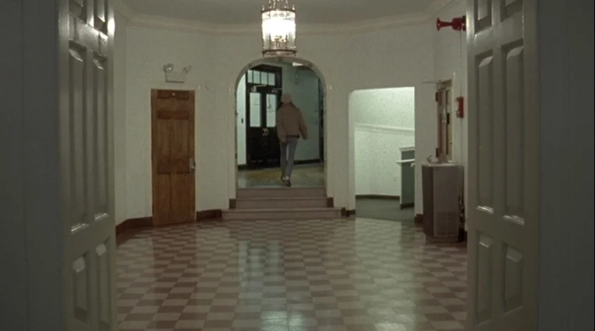 The House Of The Devil (2009) movie still: wide — A tiled lobby with white walls and high ceilings features a central arched passage. A lone…