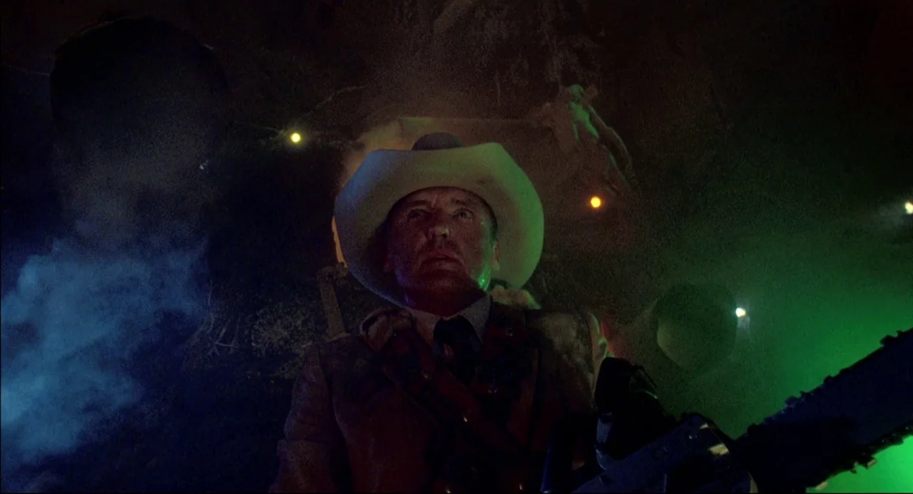 The Texas Chainsaw Massacre 2 (1986) movie still: medium — A dark subterranean tunnel features rocky, jagged walls and localized green neon light…