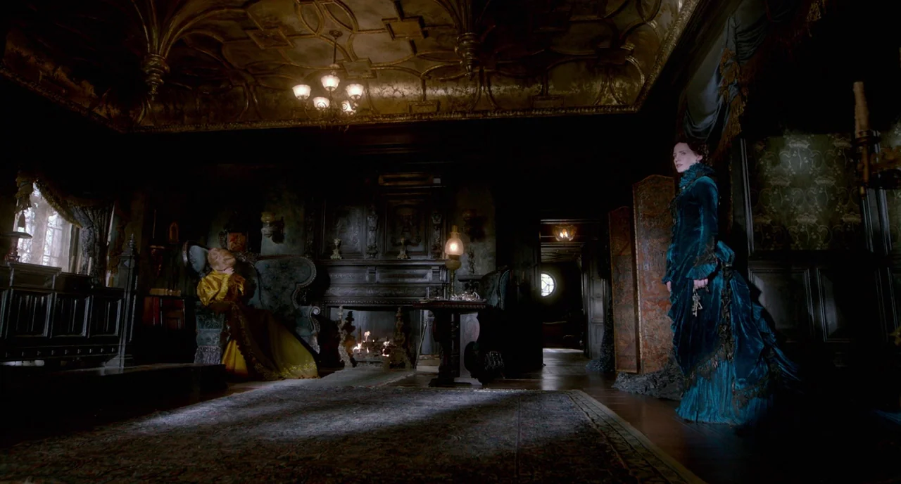 Crimson Peak (2015) movie still: wide — A dark Victorian parlor features ornate gold-leaf ceilings and heavy dark wooden paneling. One woman stands…