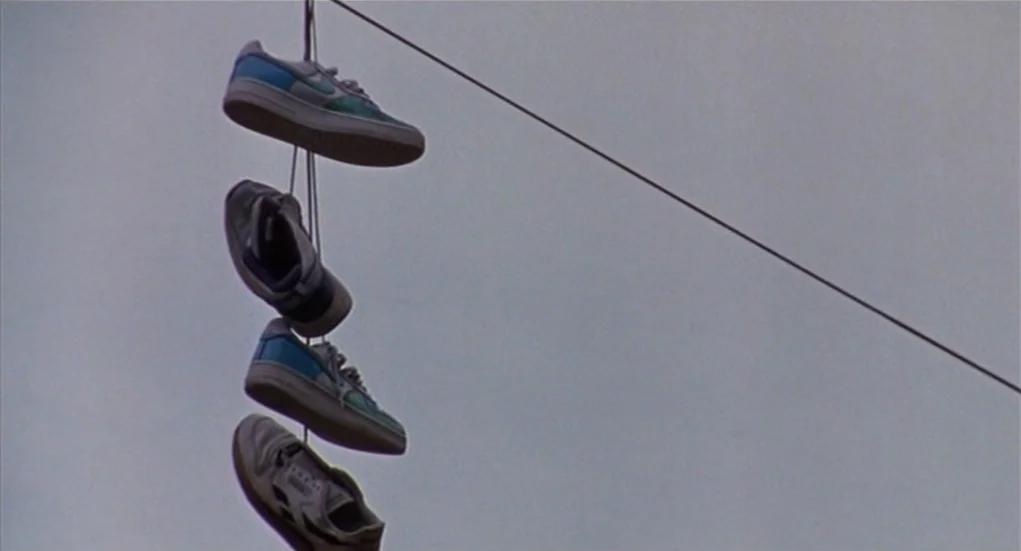 The Heart Is Deceitful Above All Things (2004) movie still: closeup — Four sneakers hang by their tied laces from a thick black utility wire. The…