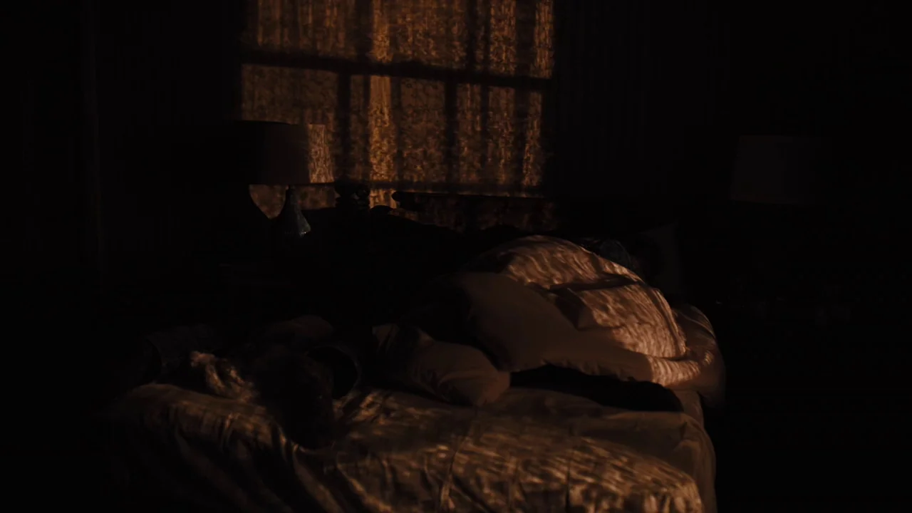 Prisoners (2013) movie still: medium — A dark bedroom at night features a bed covered in textured, folded linens. Warm light patterns from a…
