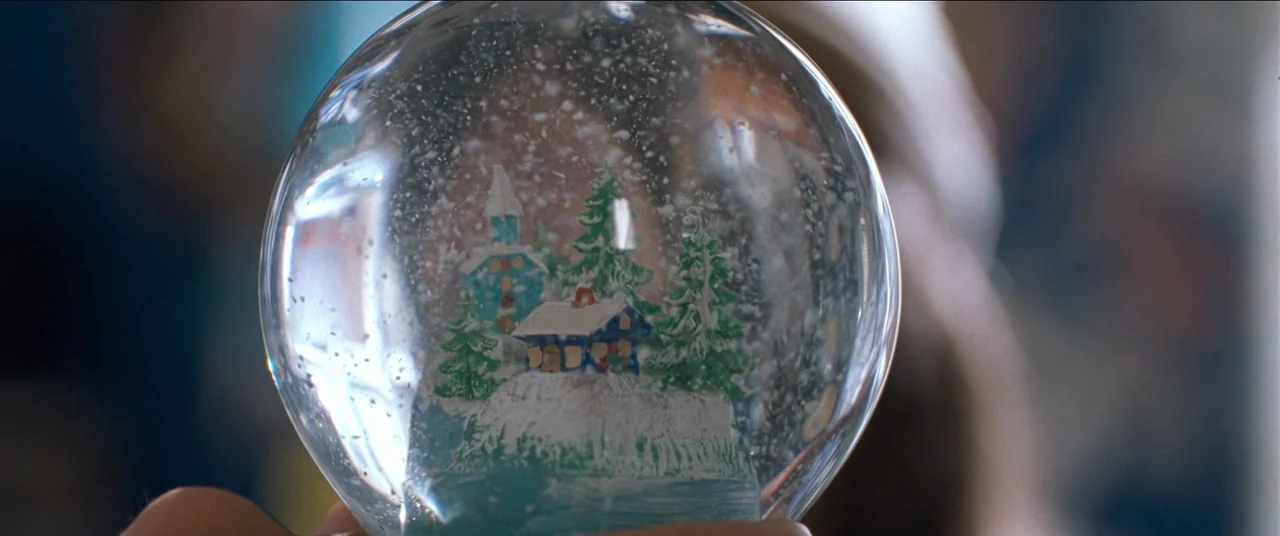 True Lies (1994) movie still: closeup — A close-up view focuses on a transparent glass snow globe containing a miniature winter landscape. Small…