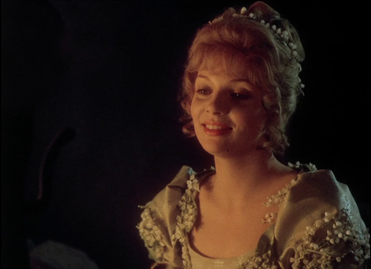 Beauty and the Beast (1979) movie still: medium — A woman stands in a dark space, her upper torso framed against a black background. She wears a…