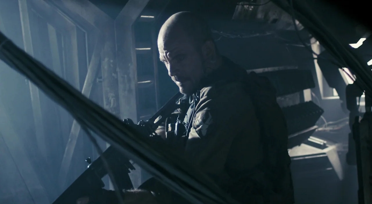 District 9 (2009) movie still: medium — A dark, cramped military transport vehicle interior filled with light smoke and metallic structural beams. A…