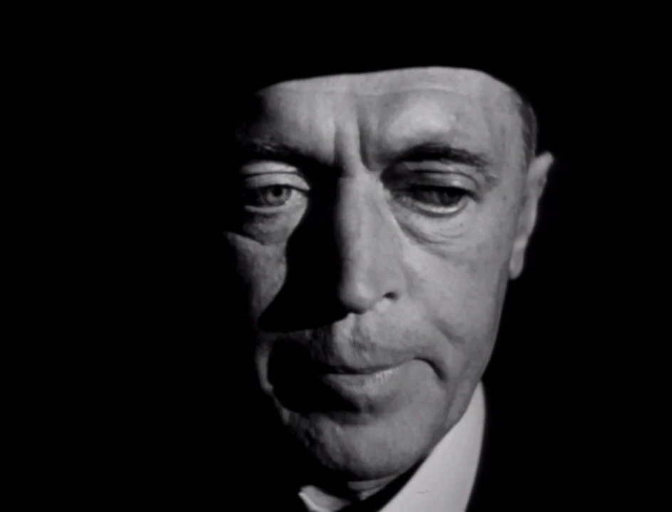 The Stranger (1946) movie still: closeup — A man's face is centered against a pitch-black background with high-contrast lighting. The subject…