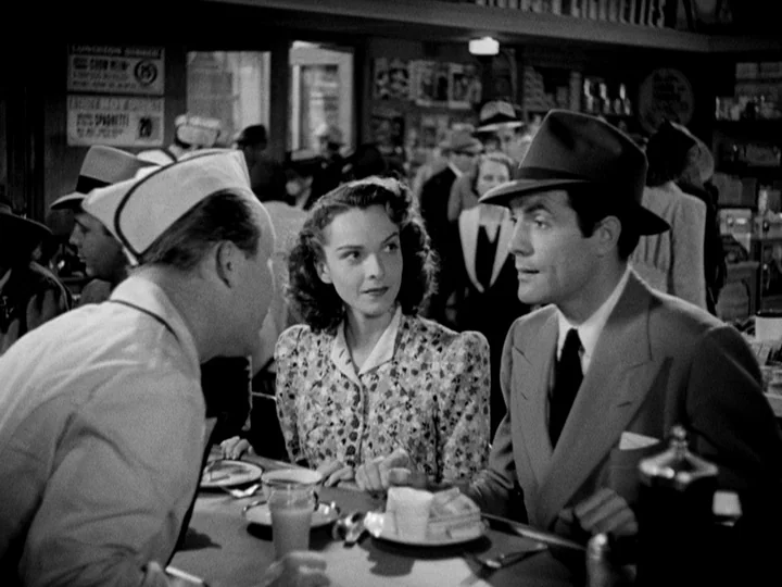 Stranger on the Third Floor (1940) movie still: medium — A crowded 1940s diner interior with patrons visible in the blurred background. A couple…