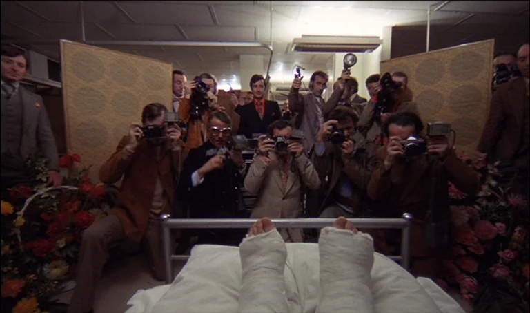 A Clockwork Orange (1971) movie still: wide — A crowded hospital room is filled with photographers holding cameras with large flash attachments. The…