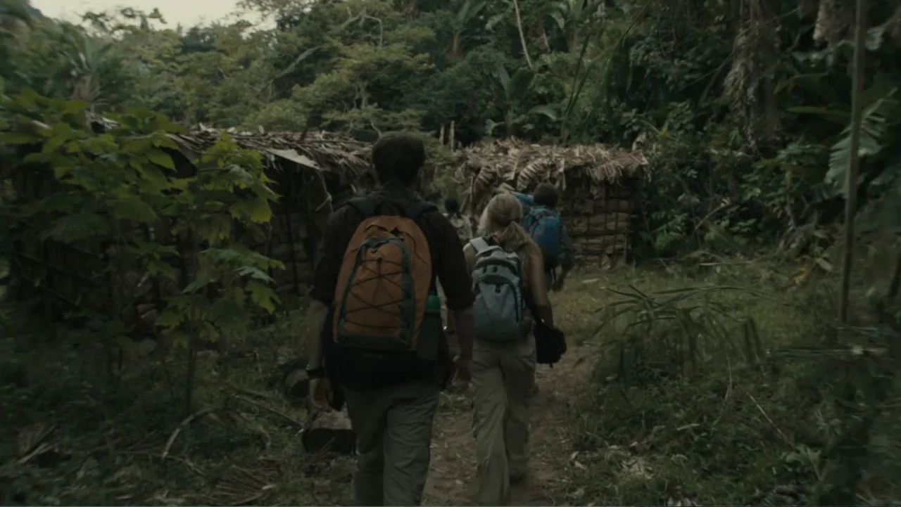 The Dinosaur Project (2012) movie still: medium — A narrow dirt path winds between rustic shelters made of woven dried palm leaves. A group of…