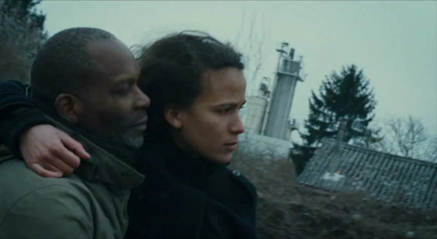 35 Shots of Rum (2008) movie still: medium — An industrial landscape features a tall concrete tower in the distant, overcast background. A man and a…