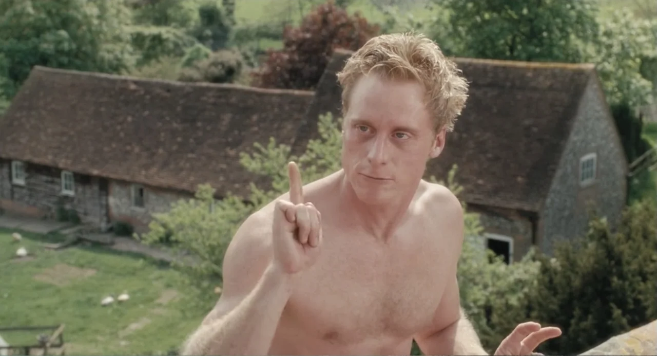 Death at a Funeral (2010) movie still: medium — A rustic farmyard features a long timber-framed barn with a red tile roof. A muscular, shirtless man…