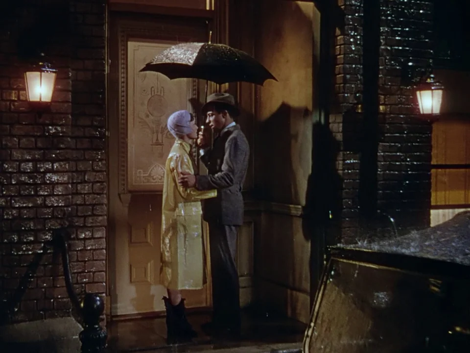 Singin’ in the Rain (1952) movie still: fullbody — A rain-slicked brick building entrance features a central door flanked by glowing lanterns. A…