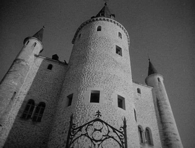 Mr. Arkadin (1955) movie still: establishing — A stone castle with multiple towers and a textured facade dominates the frame. An iron gate stands in…
