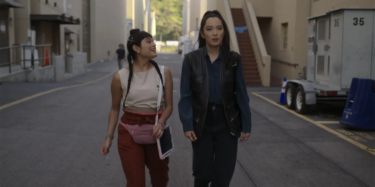 A Hollywood Christmas (2022) movie still: fullbody — An outdoor alleyway between tall commercial buildings with a concrete surface and stairs. Two…