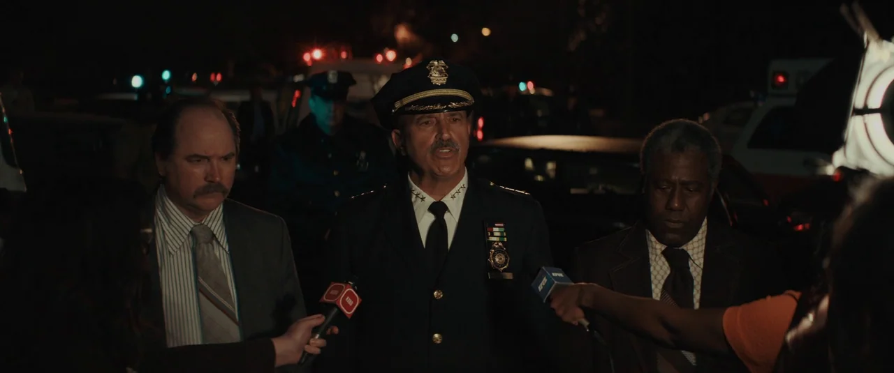 The Black Phone (2021) movie still: medium — An outdoor night scene at a police cordon with reporters surrounding three officials. The officials…