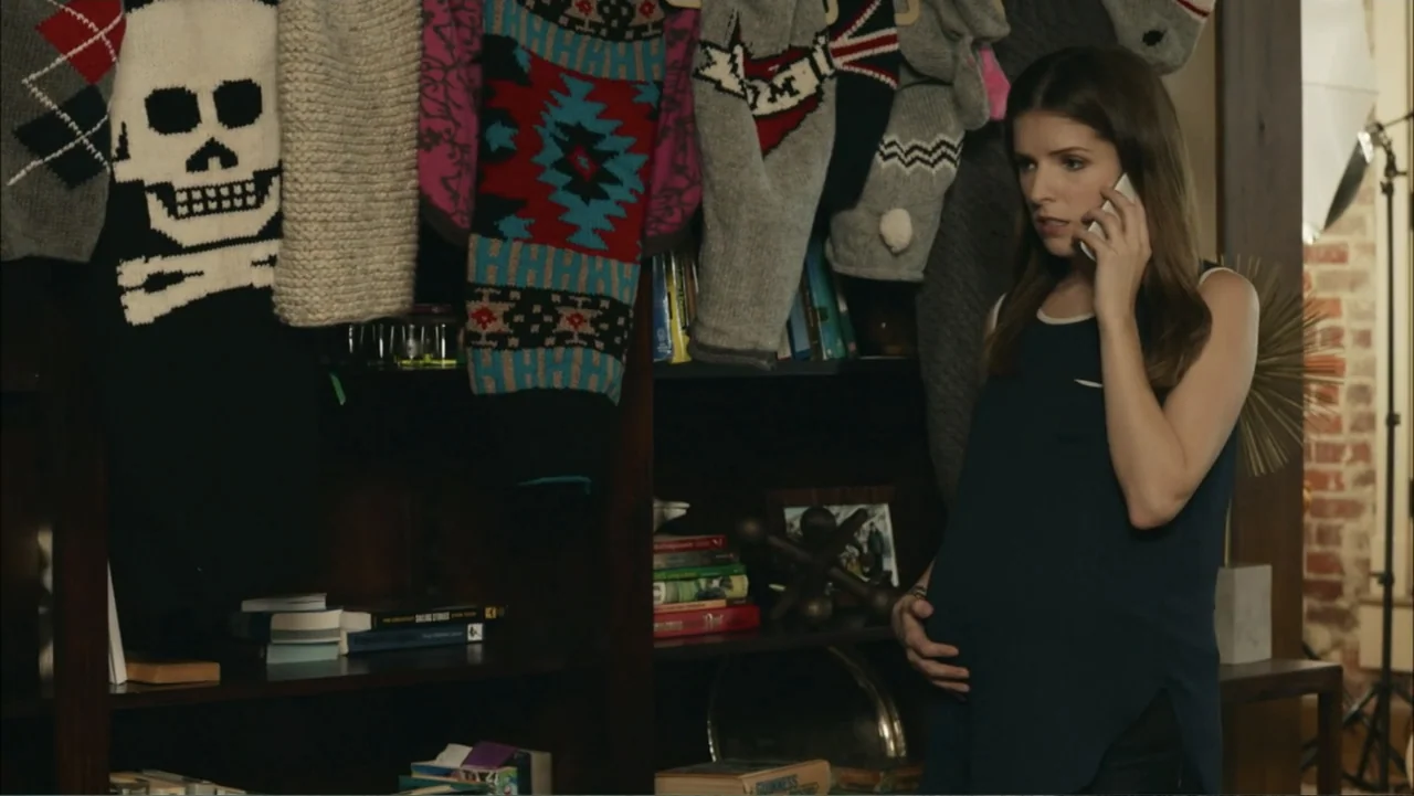The Hollars (2016) movie still: medium — A living room interior features a bookshelf decorated with colorful sweaters and books. A pregnant woman in…