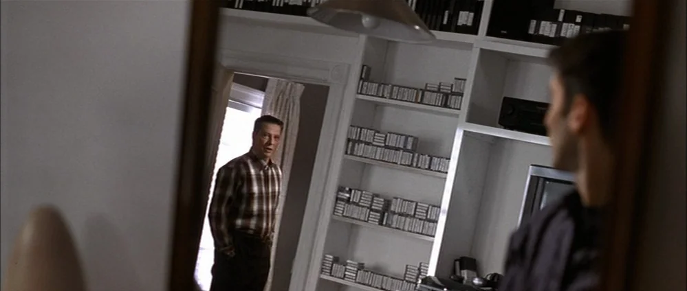 American Beauty (1999) movie still: medium — A man in a plaid shirt stands in a doorway looking into a room. The room contains floor-to-ceiling…