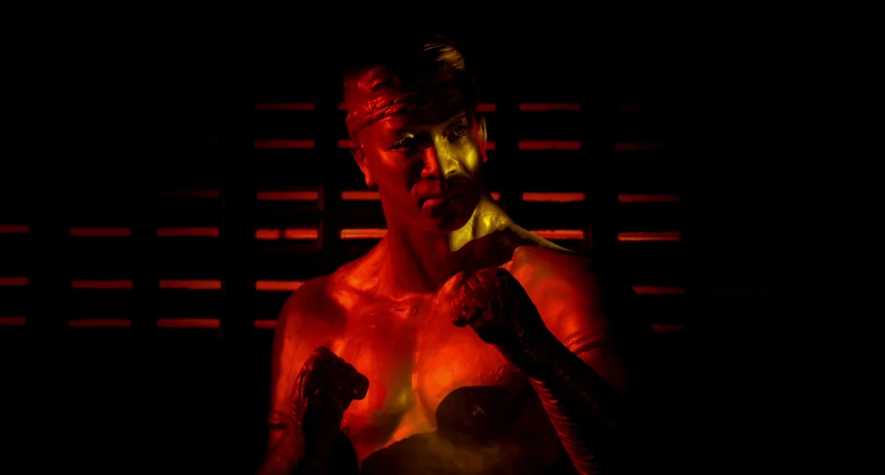 Only God Forgives (2013) movie still: medium — A dimly lit space features horizontal wall slats emitting red light behind a fighter. The man stands…
