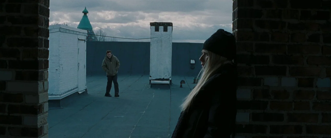 Two Lovers (2008) movie still: wide — A flat rooftop under a gray overcast sky features brick structures and vents. A blonde woman leans against a…