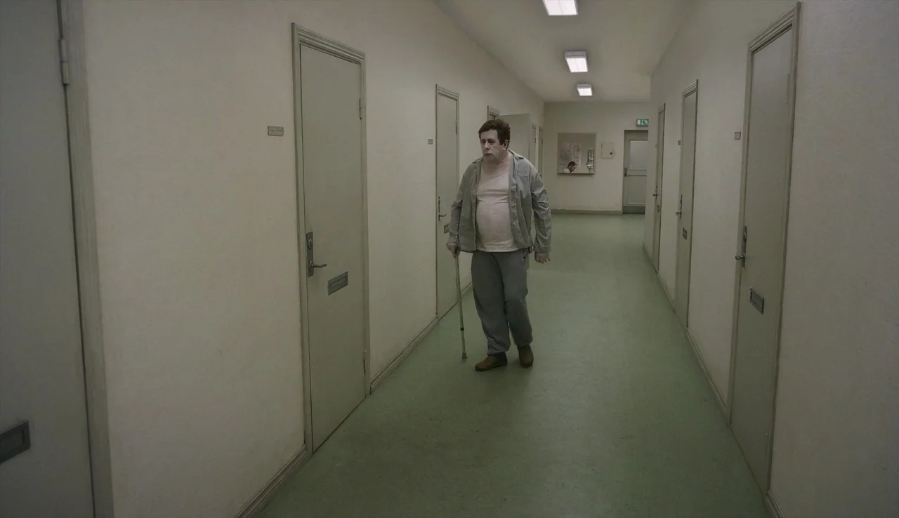 A Pigeon Sat on a Branch Reflecting on Existence (2014) movie still: fullbody — An institutional hospital corridor with multiple closed doors and…