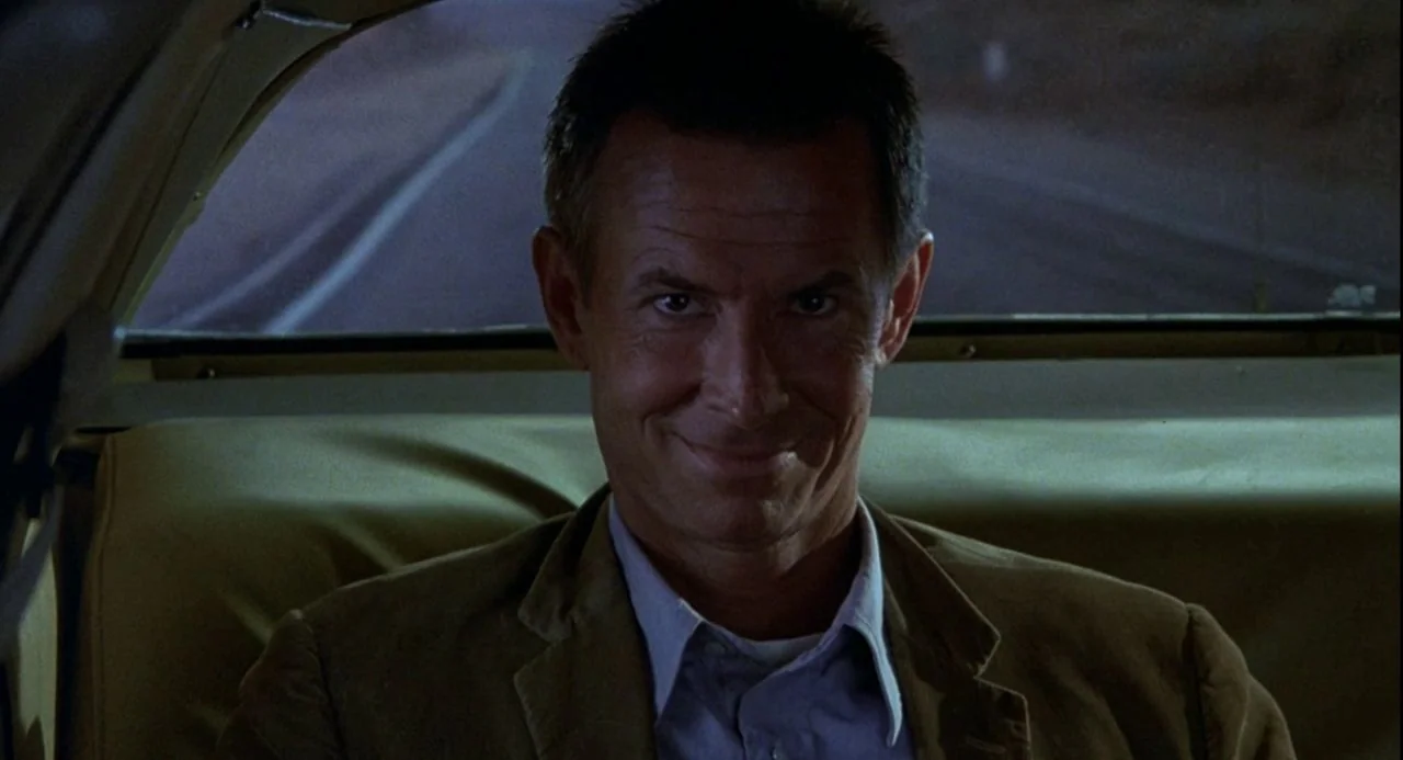 Psycho III (1986) movie still: closeup — The interior of a moving car at night with a blurred road visible outside. A man sits in the backseat,…