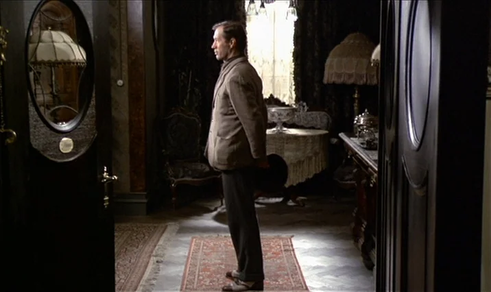 The Serpent’s Egg (1977) movie still: fullbody — A dark, wood-paneled room decorated in an early twentieth-century style with ornate lamps. A man…
