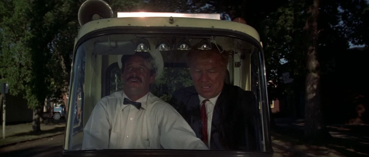 Thunderbolt & Lightfoot (1974) movie still: medium — The interior cabin of a light-colored vehicle at night with trees visible outside. Two men sit…