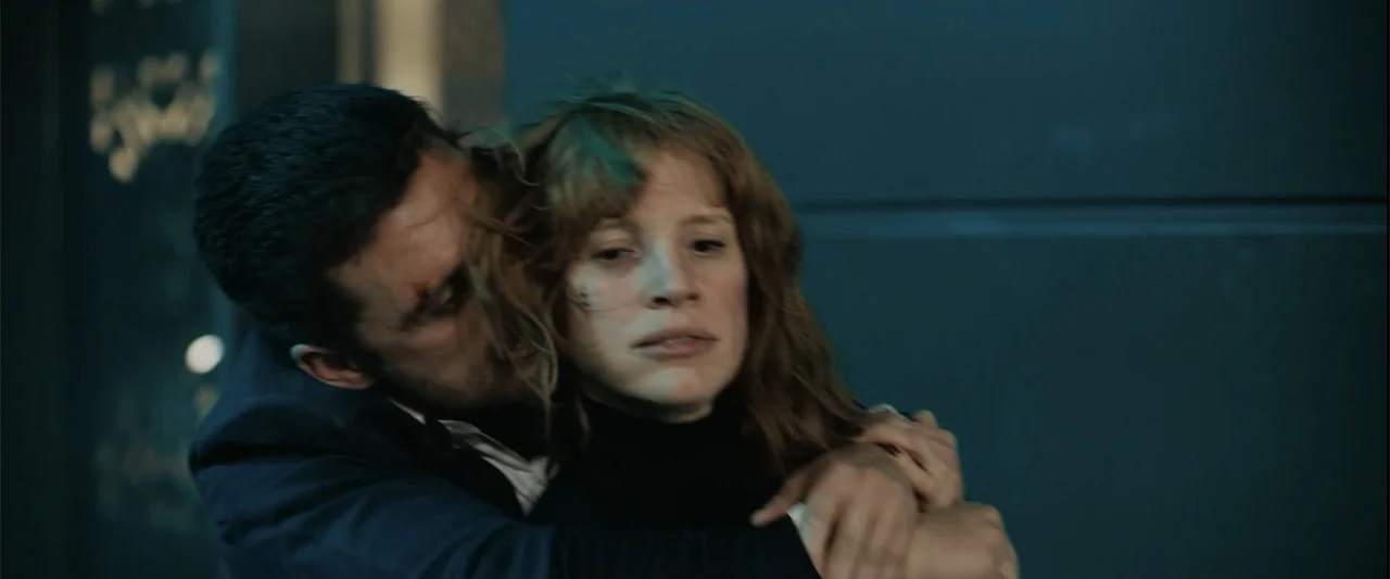 The 355 (2022) movie still: medium — A dark interior space with smooth blue wall paneling provides the background. A man holds a woman in a close…