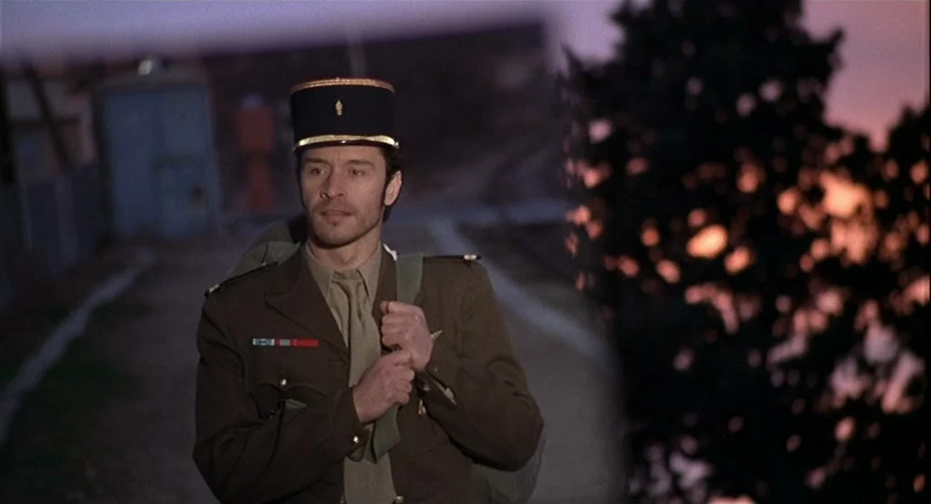 Deux (2002) movie still: medium — A rural road at dusk with a dark silhouetted tree on the right. A military man in uniform walks forward along the…