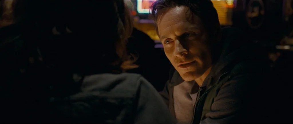 Shame (2011) movie still: medium — A dimly lit restaurant booth at night with dark surroundings. A man sits across from another person while facing…