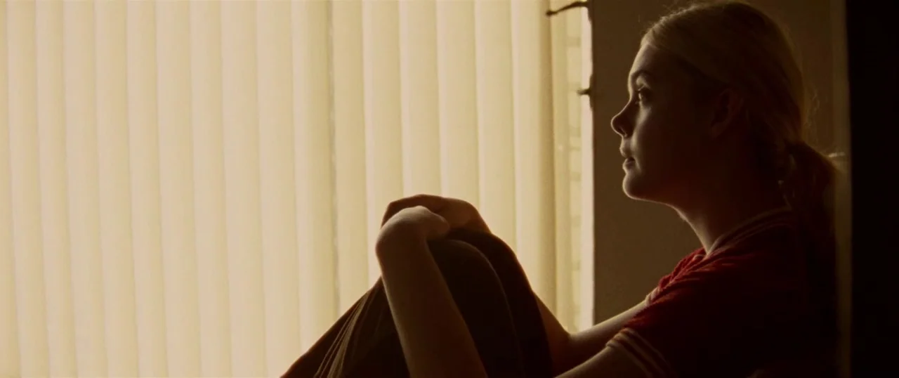 Low Down (2014) movie still: medium — A person sits next to white vertical blinds illuminated by bright daylight. The subject faces the window with…