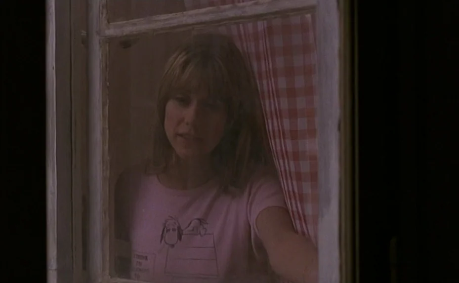 Love on the Run (1979) movie still: medium — A woman stands behind a window pane with a red and white checkered curtain. She peers outward through…