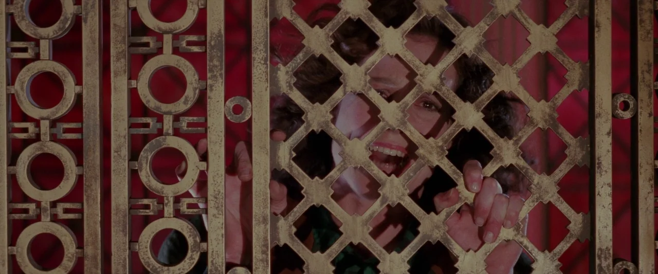 Ghostbusters 2 (1989) movie still: closeup — An Art Deco elevator gate with intricate geometric metalwork occupies the foreground of the frame. A…