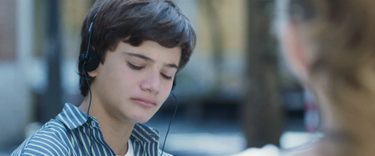 Voy a pasármelo bien (2022) movie still: closeup — An outdoor area with blurred greenery in the background providing depth. A teenage boy sits with…