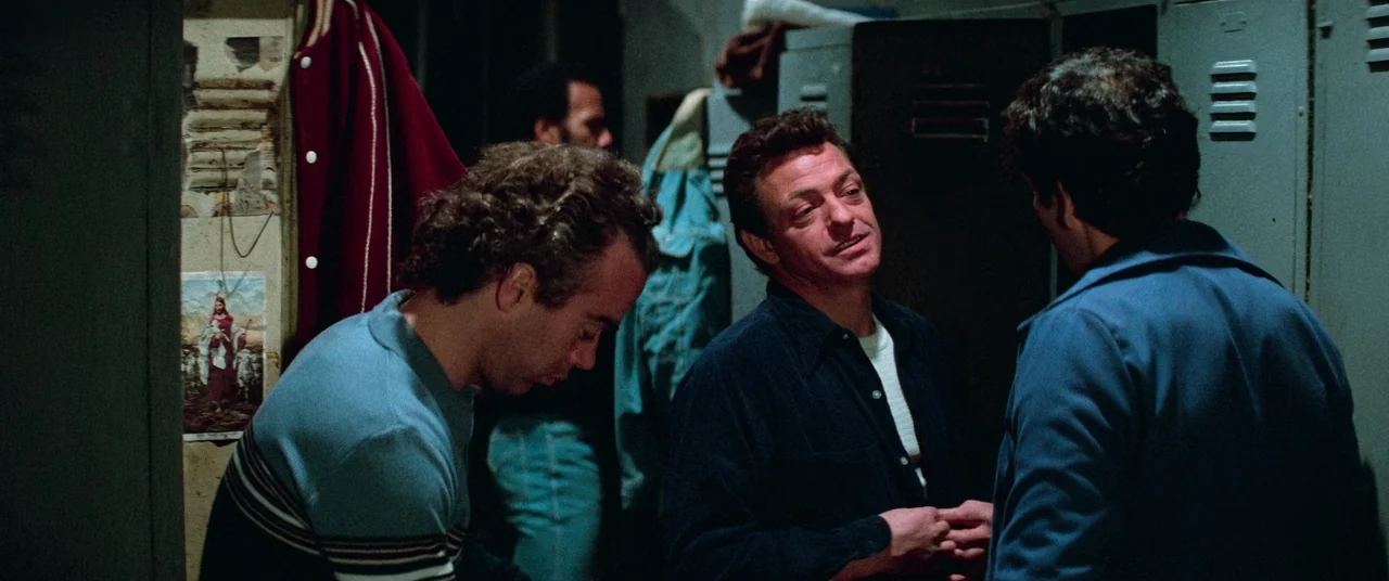 Vigilante (1982) movie still: medium — Three men stand before metal lockers in a cramped, dimly lit sports training area. The men converse while…